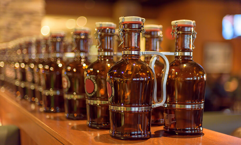 two rows of growlers ready to be filled with beer from a keg